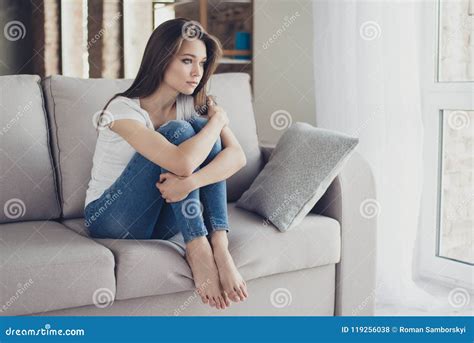 Young Pretty Lonely Sad Girl Sitting On Sofa And Hugging Her Knees