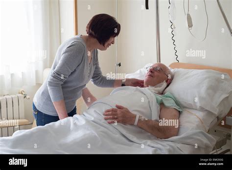 Senior Woman Caring For Husband In Hospital Recovering After Surgery