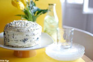 A Cake Sitting On Top Of A White Plate Next To A Vase With Yellow Flowers