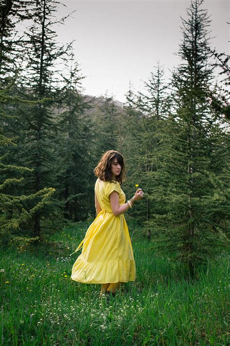 Young Woman Wearing Yellow Dress In The Woods And Holding A Dandelion