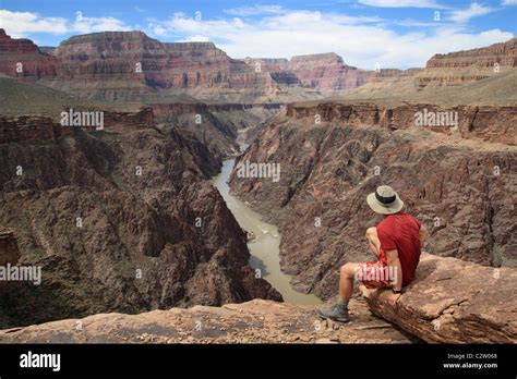 A Man Sitting On An Overlook In The Grand Canyon Looking Down Into