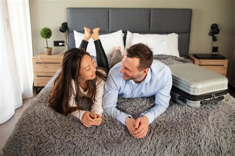Couple Vacationers Lying On Bed With Suitcase In Hotel Room On Vacation