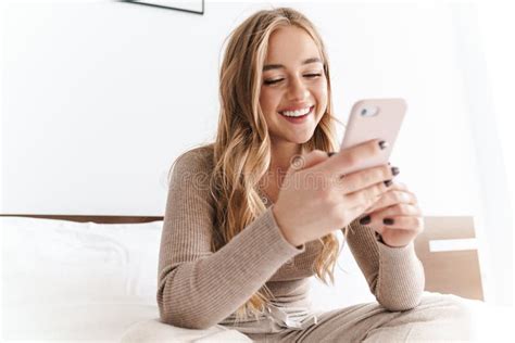 Photo Of Young Happy Woman Smiling And Using Cellphone While Sitting