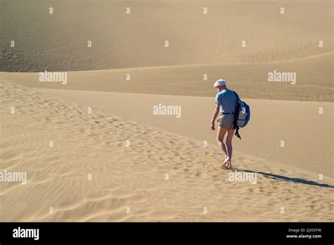 A Man Walking In The Desert An Elderly Man With A Backpack And Shorts