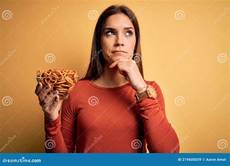 Young Beautiful Brunette Woman Holding Bowl With Germany Baked Pretzels Serious Face Thinking