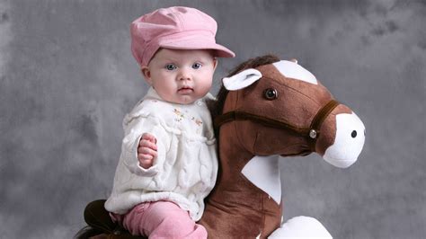 Cute Baby Is Sitting On Toy Horse Wearing White Top And