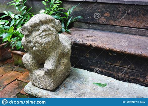 Weathered Ancient Stone Guardian Lion Statue Beside A Wooden Doorstep