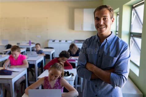 Male School Teacher Standing In An Elementary School Classroom With A