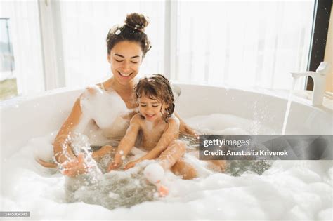 Young Mother And Little Daughter Having Fun In Bath With Foam At Home