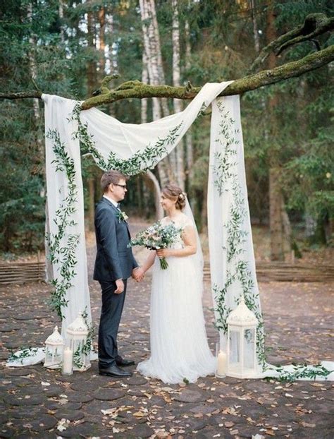 A Bride And Groom Are Standing Under An Arch Decorated With Greenery For Their Wedding Ceremony