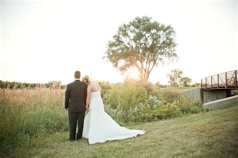 A Bride And Groom Standing In Front Of A Bridge At Sunset On Their