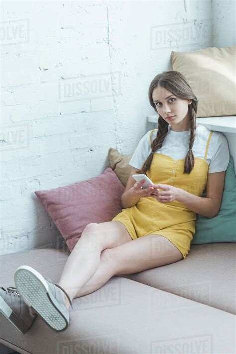 Beautiful Teen Girl With Braids Using Smartphone And Sitting On Sofa