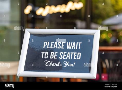 Please Wait To Be Seated Sign Standing At The Front Of A Restaurant