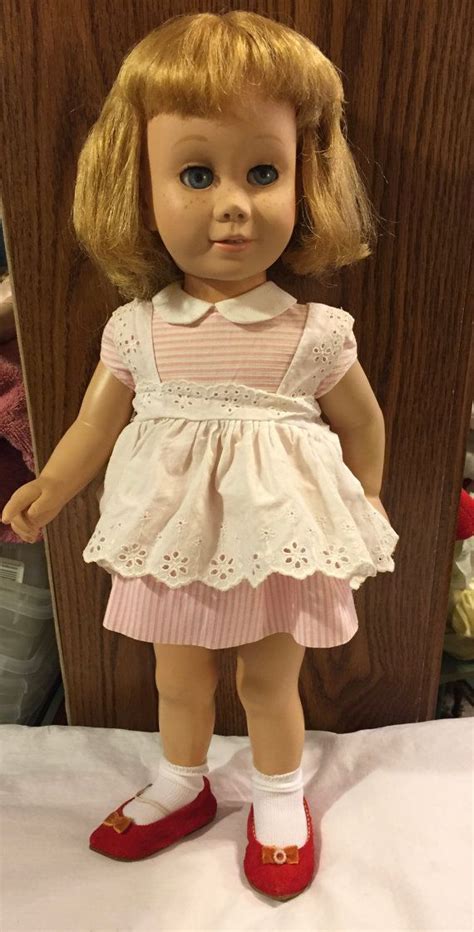 A Doll With Blonde Hair And Blue Eyes Standing Next To A Wooden Paneled