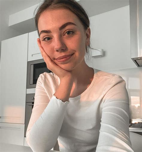 a woman sitting at a kitchen counter with her hand on her chin and looking into the camera