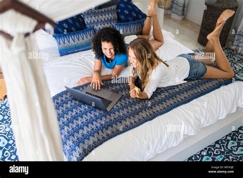 Two Smiling Women Lying In Bed Shopping Online With Credit Card And