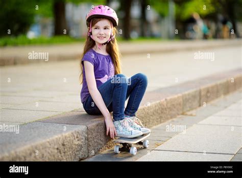 Cute Little Preteen Girl Wearing Helmet Sitting On A Skateboard In Beautiful Summer Park Stock