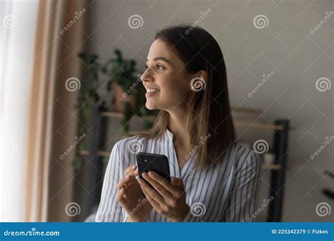 Dreamy Beautiful Woman Holding Smartphone Standing Indoor Looks Out