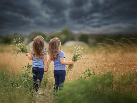 Twin Girls Holding Flowers While Looking Up At Dark Clouds
