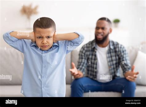 Black Boy Covering Ears While Angry Father Shouting At Home Stock Photo