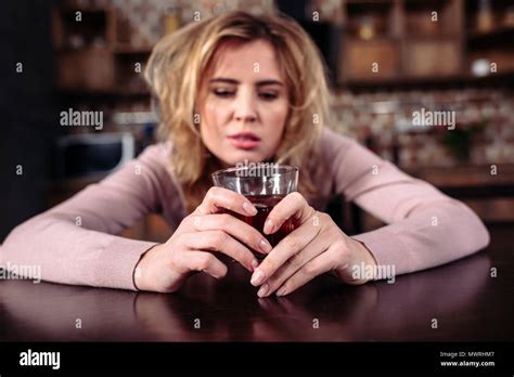 Portrait Of Drunk Woman With Glass Of Alcohol Sitting T Table At Home