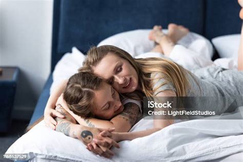 Two Lesbians Holding Hands And Embracing While Lying On Bed In Morning