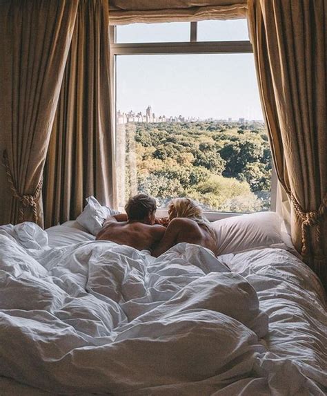 Two People Are Laying In Bed Looking Out The Window