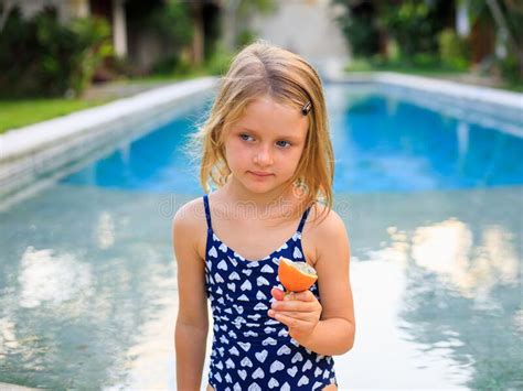 Cute Blond Little Girl In Blue Swimsuit Sitting At The Swimming Pool