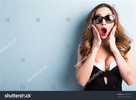 Sexy Woman In Sunglasses With Facial Expression Of Surprise Close Up Standing Over Blue