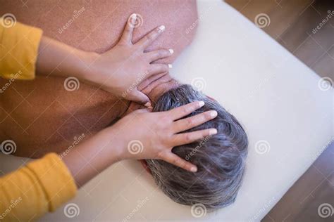 Rear View Of Shirtless Senior Male Patient Lying On Bed Receiving Neck Massage From Female