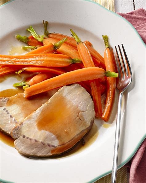 A White Plate Topped With Meat Carrots And Gravy Next To A Fork