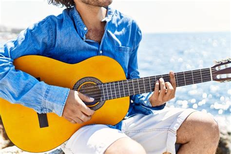 Man Playing Classical Guitar Sitting On Rock At The Beach Stock Photo