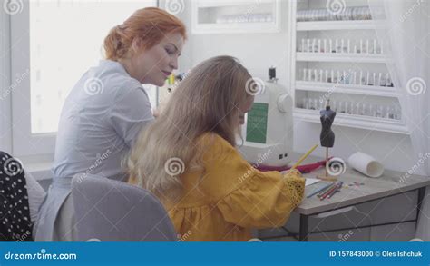Adorable Small Girl Drawing Sitting At The Table In The Foreground While Her Red Haired Mother