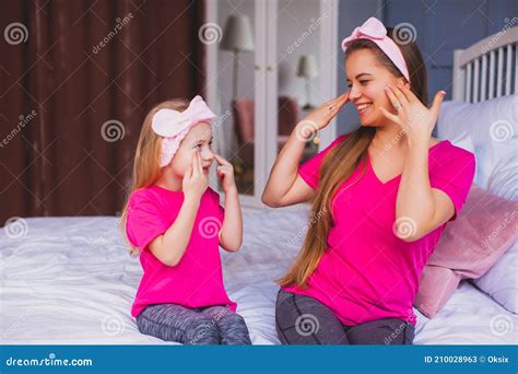 Girl And Her Mom Sitting On The Bed And Make Face Care Stock Image