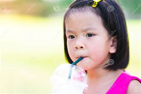 Cute Asian Girl Sucking Water From A Plastic Glass With A Green Straw