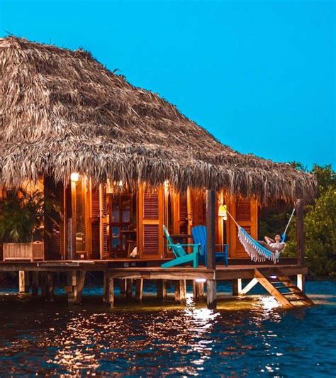 A Hut On The Water With A Hammock Hanging From Its Roof