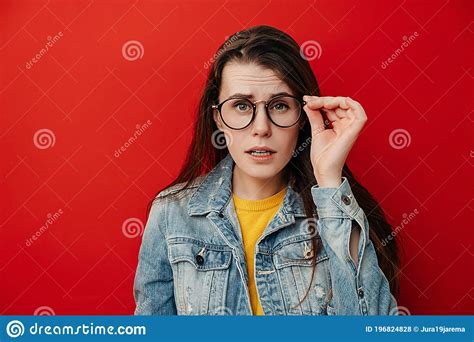 Shocked Emotional Young Woman Keeps Hand On Rim Of Spectacles Dressed