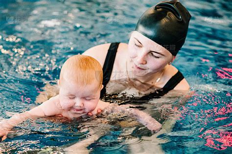 让婴儿在嬉水池中潜水。年轻的母亲，游泳教练和快乐的小女孩在游泳池里。幼儿学游泳。享受在水里游泳的第一