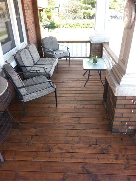 Two Chairs And A Table On A Wooden Porch With Brick Pillars Glass