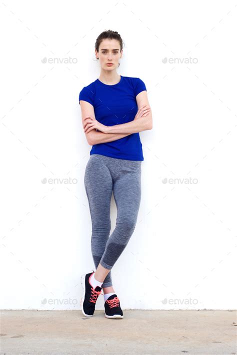 Sporty Woman Leaning Against White Wall With Arms Crossed Stock Photo
