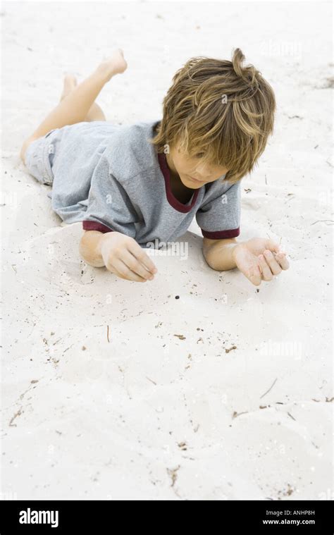 Boy Lying On Stomach In Sand With Legs Up Looking Down Stock Photo Alamy