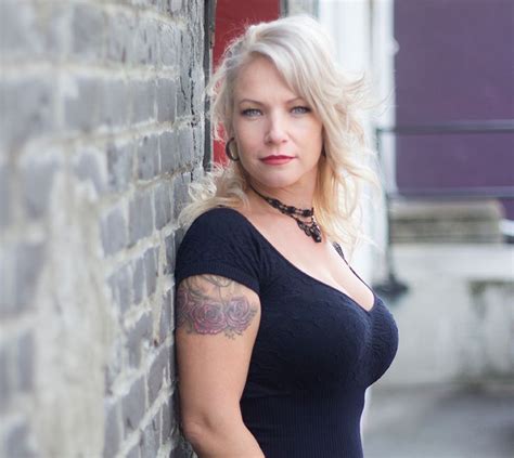 A Woman Leaning Against A Brick Wall With A Tattoo On Her Left Arm And
