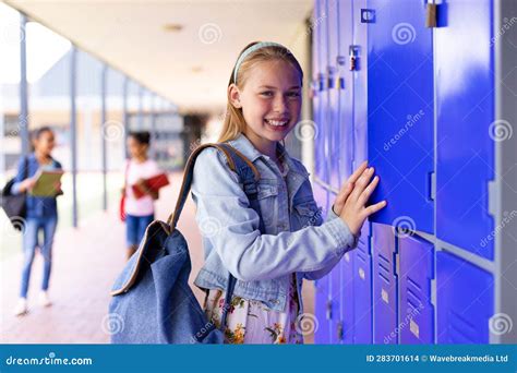 Portrait Of Happy Caucasian Schoolgirl Standing Next To Lockers In Corridor At School Stock
