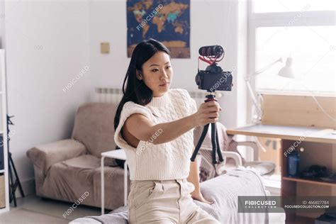 Serious Ethnic Female Vlogger Recording Video On Photo Camera While Standing In Living Room