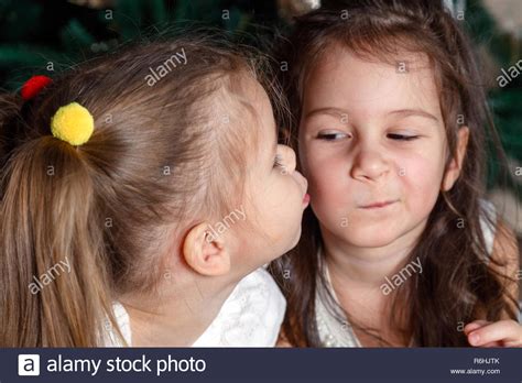 two cute sisters of the same age lie next to the new year tree one kisses the other on the