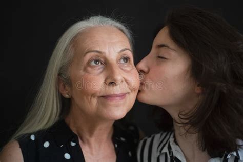 Portrait Of Senior Grandmother With Her Granddaughter Kissing Her Over Black Blackground Stock