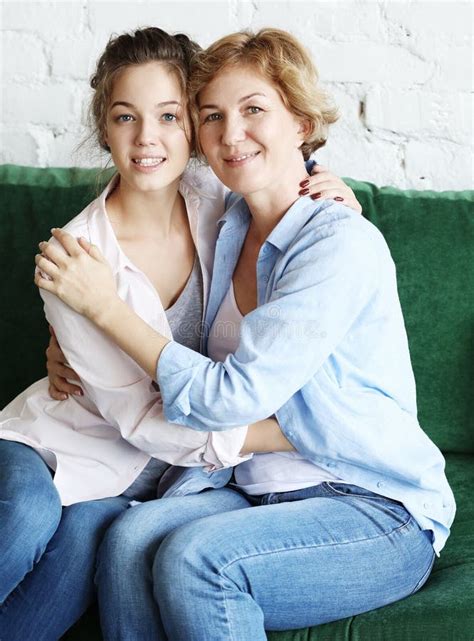 beautiful senior mom and her adult daughter are hugging looking at camera and smiling stock