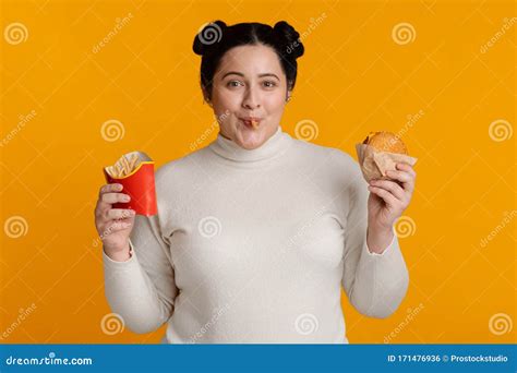 Funny Fat Girl Eating Burger And French Fries On Yellow Background