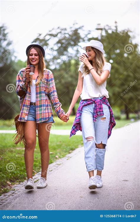 Two Young Women Holding Hands Walking In Green Park Best Friends Stock