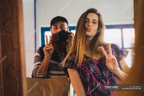 Young Man Taking Selfie With Woman Gesturing Two Fingers At Mirror